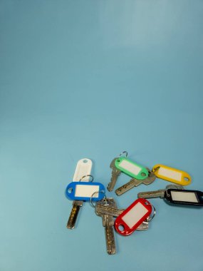 Açık mavi arkaplanda izole edilmiş renkli anahtarlıklara sahip birkaç anahtar.