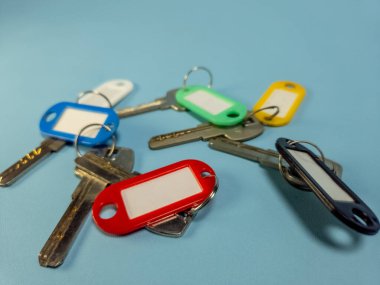 Açık mavi arkaplanda izole edilmiş renkli anahtarlıklara sahip birkaç anahtar.