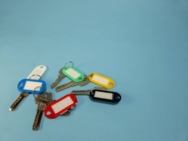 Açık mavi arkaplanda izole edilmiş renkli anahtarlıklara sahip birkaç anahtar.