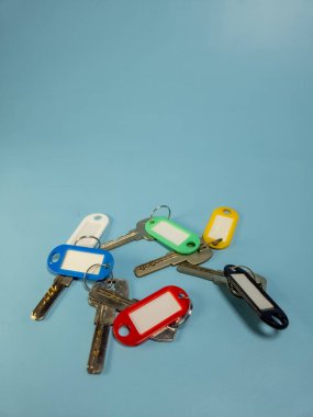Açık mavi arkaplanda izole edilmiş renkli anahtarlıklara sahip birkaç anahtar.