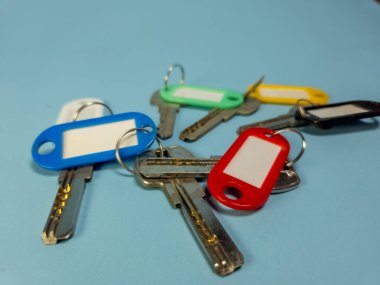 Açık mavi arkaplanda izole edilmiş renkli anahtarlıklara sahip birkaç anahtar.