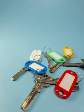 Açık mavi arkaplanda izole edilmiş renkli anahtarlıklara sahip birkaç anahtar.