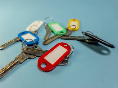 Açık mavi arkaplanda izole edilmiş renkli anahtarlıklara sahip birkaç anahtar.