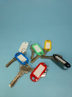 Açık mavi arkaplanda izole edilmiş renkli anahtarlıklara sahip birkaç anahtar.