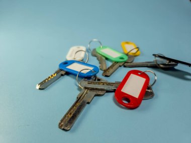Açık mavi arkaplanda izole edilmiş renkli anahtarlıklara sahip birkaç anahtar.