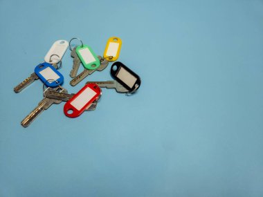 Açık mavi arkaplanda izole edilmiş renkli anahtarlıklara sahip birkaç anahtar.