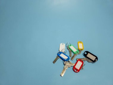 Açık mavi arkaplanda izole edilmiş renkli anahtarlıklara sahip birkaç anahtar.