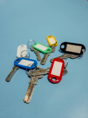 Açık mavi arkaplanda izole edilmiş renkli anahtarlıklara sahip birkaç anahtar.