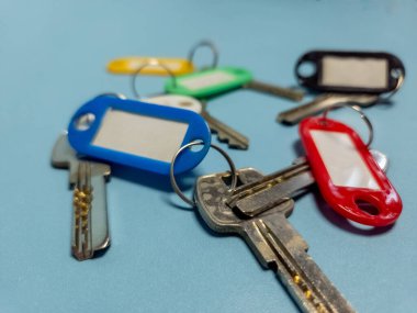 Açık mavi arkaplanda izole edilmiş renkli anahtarlıklara sahip birkaç anahtar.