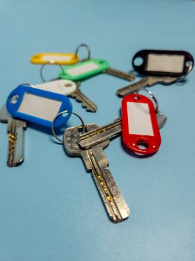 Açık mavi arkaplanda izole edilmiş renkli anahtarlıklara sahip birkaç anahtar.