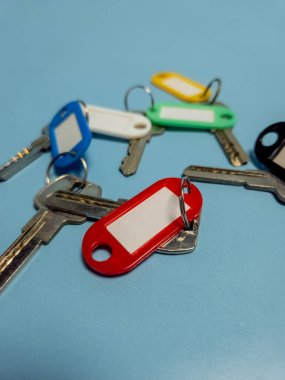 Açık mavi arkaplanda izole edilmiş renkli anahtarlıklara sahip birkaç anahtar.