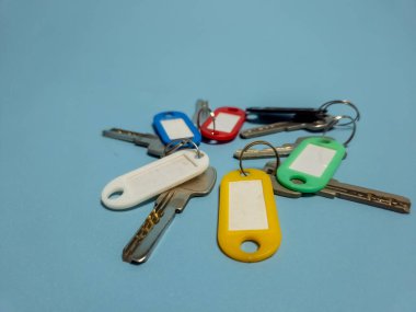 Açık mavi arkaplanda izole edilmiş renkli anahtarlıklara sahip birkaç anahtar.