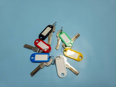 Açık mavi arkaplanda izole edilmiş renkli anahtarlıklara sahip birkaç anahtar.