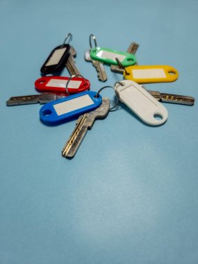 Açık mavi arkaplanda izole edilmiş renkli anahtarlıklara sahip birkaç anahtar.
