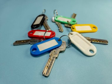 Açık mavi arkaplanda izole edilmiş renkli anahtarlıklara sahip birkaç anahtar.