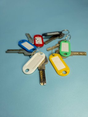 Açık mavi arkaplanda izole edilmiş renkli anahtarlıklara sahip birkaç anahtar.