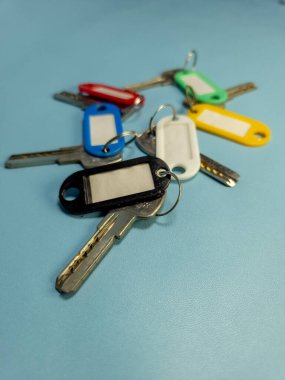 Açık mavi arkaplanda izole edilmiş renkli anahtarlıklara sahip birkaç anahtar.