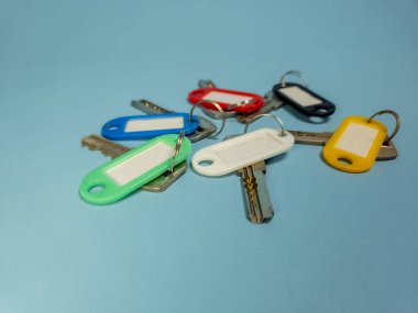Açık mavi arkaplanda izole edilmiş renkli anahtarlıklara sahip birkaç anahtar.