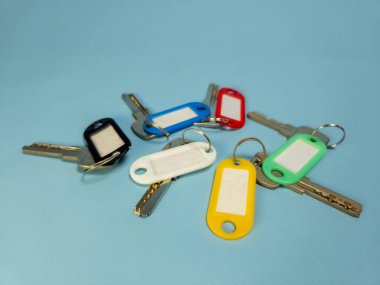 Açık mavi arkaplanda izole edilmiş renkli anahtarlıklara sahip birkaç anahtar.