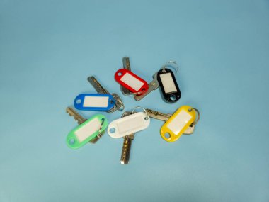 Açık mavi arkaplanda izole edilmiş renkli anahtarlıklara sahip birkaç anahtar.
