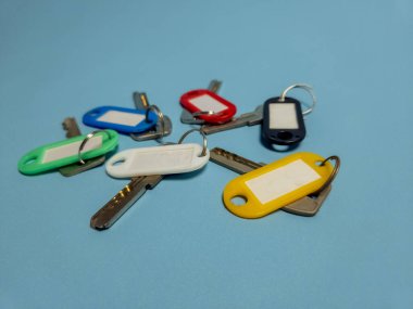 Açık mavi arkaplanda izole edilmiş renkli anahtarlıklara sahip birkaç anahtar.