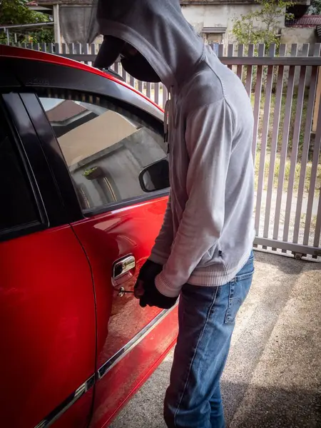 Bir hırsızın evde park etmiş bir arabanın kapısını açtığı görüntüsü.