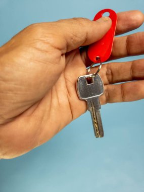 Bir adam, açık mavi arka planda izole edilmiş anahtarlığı olan bir kapı anahtarı tutuyor.