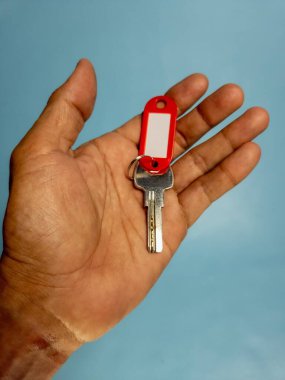 Bir adam, açık mavi arka planda izole edilmiş anahtarlığı olan bir kapı anahtarı tutuyor.