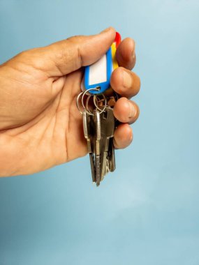 Bir adam açık mavi arka planda izole edilmiş anahtarlığı olan birkaç kapı anahtarı tutuyor.