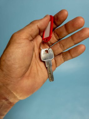 Bir adam, açık mavi arka planda izole edilmiş anahtarlığı olan bir kapı anahtarı tutuyor.