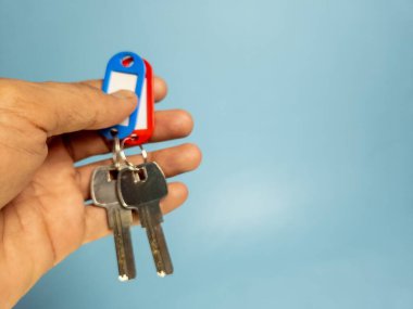 Bir adam açık mavi arka planda iki anahtar zinciri tutuyor.