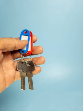 Bir adam, açık mavi arka planda izole edilmiş anahtarlığı olan bir kapı anahtarı tutuyor.