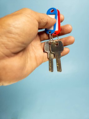 Bir adam açık mavi arka planda iki anahtar zinciri tutuyor.