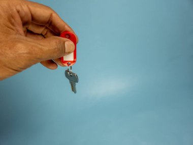 Bir adam, açık mavi arka planda izole edilmiş anahtarlığı olan bir kapı anahtarı tutuyor.