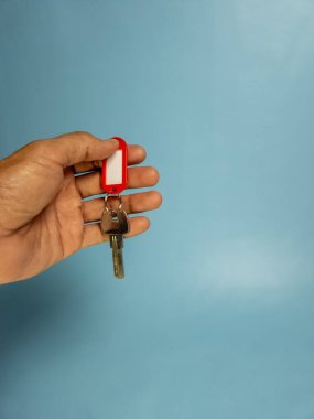 Bir adam, açık mavi arka planda izole edilmiş anahtarlığı olan bir kapı anahtarı tutuyor.