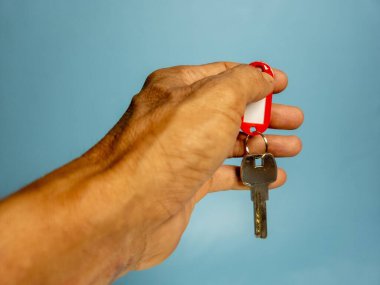 Bir adam, açık mavi arka planda izole edilmiş anahtarlığı olan bir kapı anahtarı tutuyor.