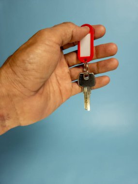 Bir adam, açık mavi arka planda izole edilmiş anahtarlığı olan bir kapı anahtarı tutuyor.