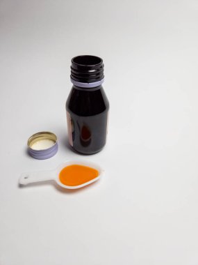 Açık bir ilaç şişesi, içinde öksürük şurubu olan, beyaz bir arka planda izole edilmiş. Görüntü, hastalık için sağlık, tedavi ve ilaç kavramlarını iletiyor. Tıbbi ya da sağlık için kullanılabilir..