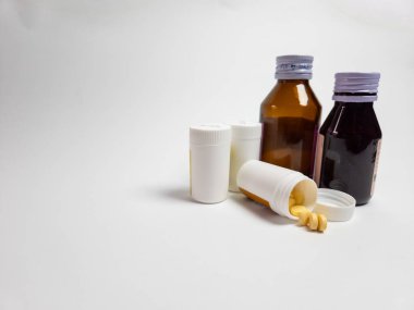 Beyaz bir yüzeyde sergilenen haplar ve şişelerdeki sıvı ilaçlar da dahil olmak üzere çeşitli ilaçlar. Kompozisyon, sağlık hizmetleri ve ilaçların vurgulandığı çeşitli ilaç ürünlerini yakalıyor..