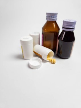 Beyaz bir yüzeye serpilmiş ilaç şişeleri ve hapların yakın çekim görüntüleri. Görüntü, sağlık, ilaç ve tedavi temalarını iletiyor. Tıbbi maddeler ya da sağlıkla ilgili içerik çizmeye elverişli.