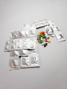 İlaç konsepti, beyaz bir yüzeye dağılmış kapsüller, farklı şekillerde haplar ve renkler içeren bir yığın açık su toplamasını gösteriyor. Sağlık ve İlaç teması.