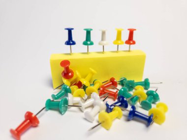 Beyaz bir yüzeye saçılmış renkli raptiyelerden oluşan bir kolleksiyon. Bazıları sarı bir blokta düzgünce düzenlenmiş. Resim değişik renkler ve şekiller sergiliyor, iğneler ilginç bir kompozisyon oluşturmak için yerleştirilmiş. Resmetmek için mükemmel 