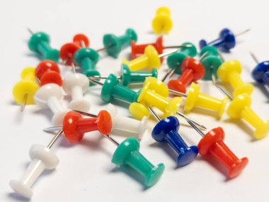 Beyaz bir yüzeye saçılmış renkli raptiye koleksiyonunun yakın çekimi. Raptiyeler kırmızı, sarı, yeşil, mavi ve beyaz olmak üzere çeşitli renklerdir. Kompozisyon iyi ışıklandırılmış, alan derinliği sığ, raptiyeler yapıyor.