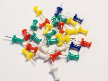 Beyaz arka planda düzenlenmiş renkli raptiye koleksiyonu. İtme iğneleri kırmızı, yeşil, sarı, mavi ve beyaz olmak üzere çeşitli renklerdir. Görüntü yukarıdan aşağıya doğru çekiliyor, iğnelerin düzenini gösteriyor. İğneler sapasağlam