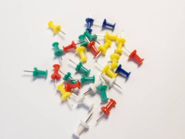 Yakından çekilen bir fotoğrafta beyaz arka plana saçılmış renkli raptiyeler sergileniyor. Resim, çeşitli renkleri ve iğnelerin keskin detaylarını vurguluyor ve varyasyonlar için görsel olarak çekici bir kompozisyon oluşturuyor.