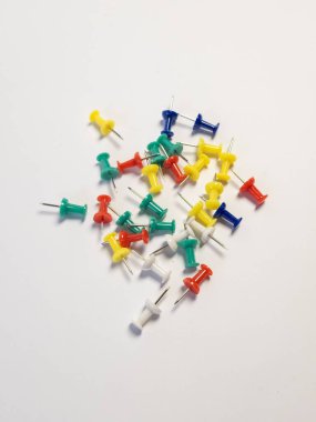 Temiz beyaz arka plana rastgele saçılmış çeşitli renkli raptiye koleksiyonu. İtme iğneleri kırmızı, yeşil, sarı, mavi ve beyaz gibi çeşitli renklerdedir. Bu resim organizasyon ve ofis malzemeleri ile ilgili kavramlar için uygundur.