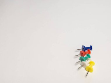 Tepeden çekimde el değmemiş beyaz bir yüzey üzerinde beş renkli iğne dizilimi sergileniyor. Mavi, kırmızı, yeşil, beyaz ve sarı raptiyeler köşegen bir çizgide konumlandırılarak görsel ilgi uyandırıyor. Temiz arkaplan yeterli kopya sp sağlar