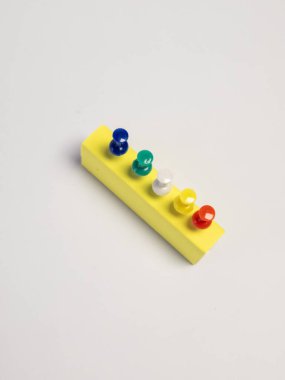 Üst üste çekilen bir stüdyo çekiminde arka arkaya beş renkli raptiyeli sarı dikdörtgen köpük bloğu yer alır. Mandallar mavi, yeşil, beyaz, sarı ve kırmızıdır. Kompozisyon, beyaz bir arkaplana karşı basit ve temizdir.