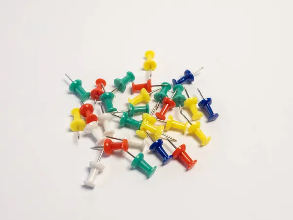 Temiz beyaz arka plana rastgele saçılmış çeşitli renkli raptiye koleksiyonu. Resimde kırmızı, yeşil, sarı, mavi ve beyaz gibi çeşitli canlı renkler yer alıyor. Yakın çekim keskin noktaları ve yuvarlak kafaları vurguluyor. 