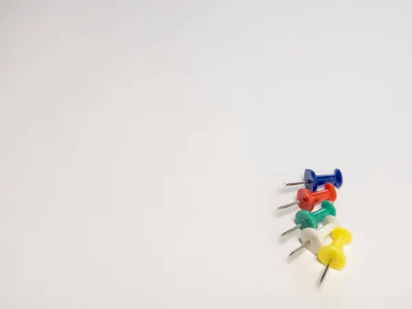 Tepeden çekimde el değmemiş beyaz bir yüzey üzerinde beş renkli iğne dizilimi sergileniyor. Mavi, kırmızı, yeşil, beyaz ve sarı raptiyeler köşegen bir çizgide konumlandırılarak görsel ilgi uyandırıyor. Temiz arkaplan yeterli kopya sp sağlar